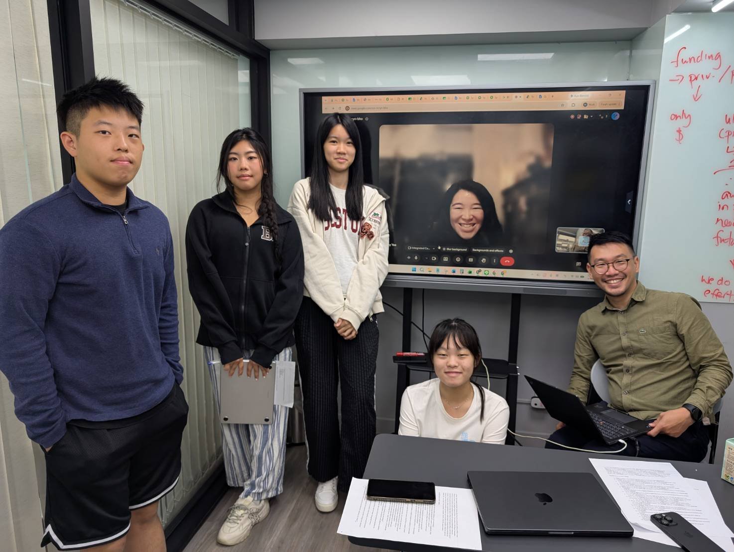 Team members interviewing Lindsey via video call, with the team gathered around a table and laptops